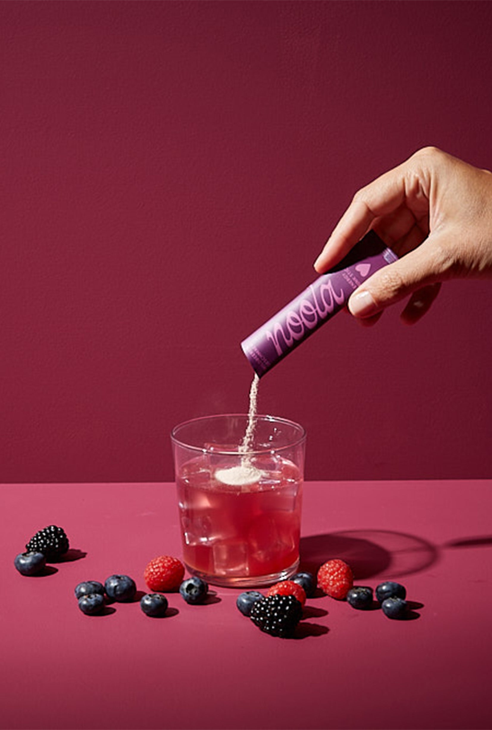 noola Energy Pulver wird in ein Glas gegeben, umgeben von frischen Beeren