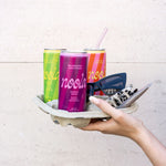 3 noola Energy Drink Dosen in Wildbeere, Pfirsich und Zitrone-Limette werden in einem Papptray von einer Hand gehalten